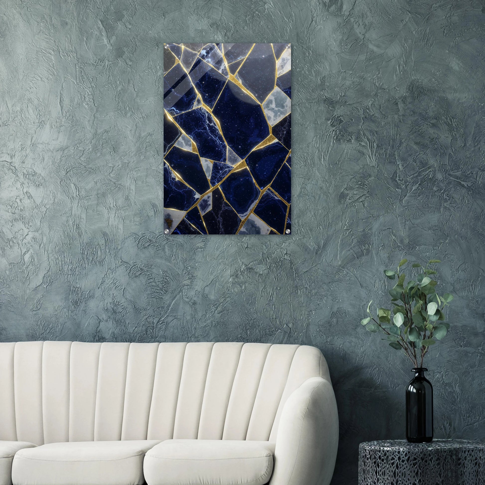 Abstract art piece on a textured wall above a sofa with a plant on a side table.